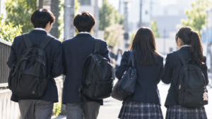 制服姿の高校生4人がリュックを背負って通学路を歩く後ろ姿