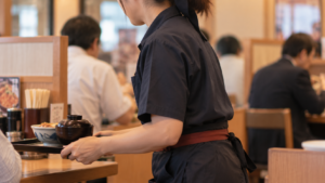 かつやでカツ丼と味噌汁をお盆で運ぶホールスタッフ