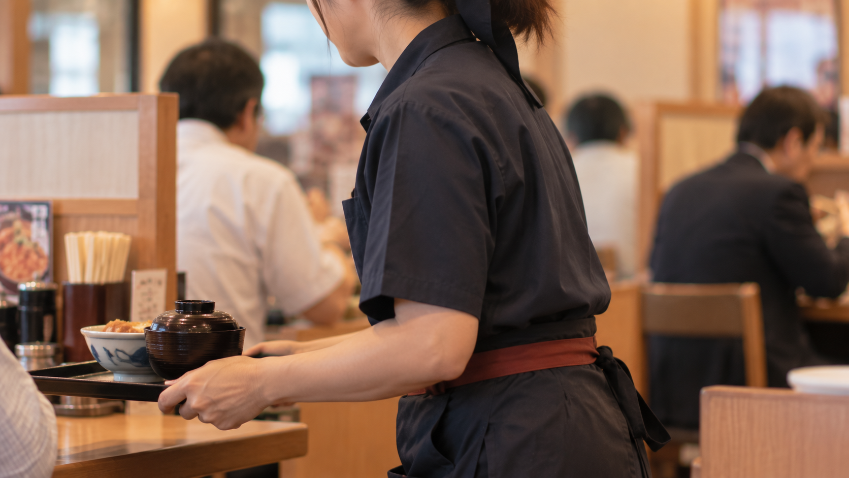 かつやでカツ丼と味噌汁をお盆で運ぶホールスタッフ